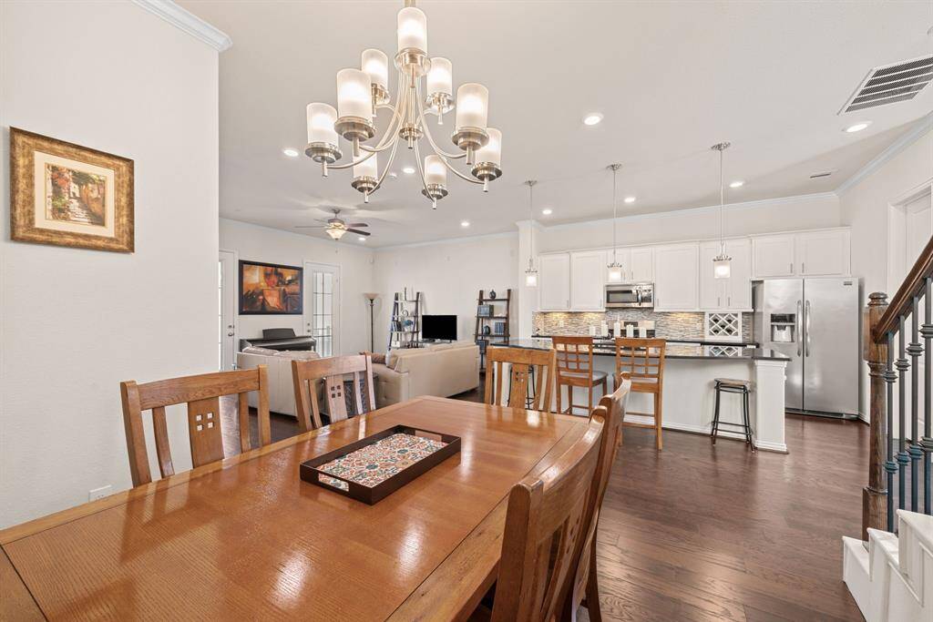 Bright and welcoming living room featuring hardwood floors, a cozy L-shaped sofa, and a ceiling fan. French doors open to a balcony, enhancing natural light. The room includes a TV setup and elegant shelving, creating a perfect space for relaxation and entertainment.