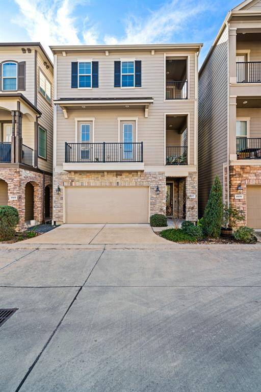 Modern three-story townhouse with a neutral facade, featuring a two-car garage and balconies. The exterior combines brick and siding, offering a clean, contemporary look. Located in a well-maintained neighborhood with paved driveways.