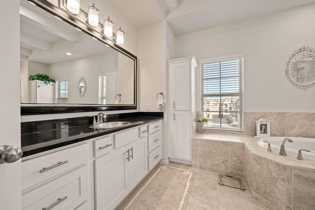 This bathroom features a spacious layout with a luxurious soaking tub, elegant tile flooring, and ample natural light from large windows. The dual-sink vanity offers plenty of storage, and the neutral tones create a serene atmosphere.