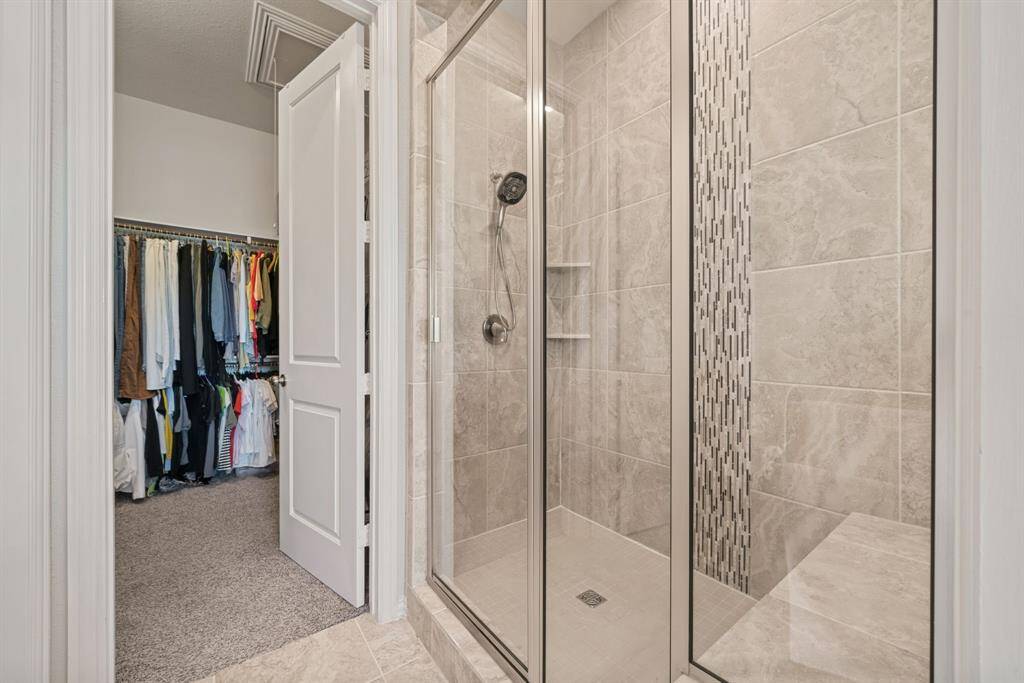 This spacious bathroom features a large soaking tub, separate glass-enclosed shower, dual sinks with ample counter space, and elegant tile flooring. It includes a walk-in closet and modern lighting, offering both luxury and functionality.
