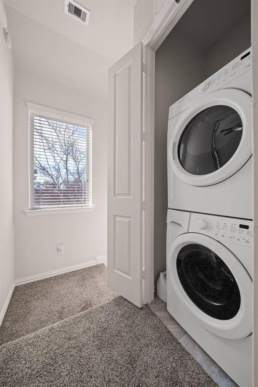 This photo shows a narrow, paved side yard with a wooden privacy fence, small plants, and an outdoor air conditioning unit. The space is adjacent to a house with siding and several windows, offering a cozy outdoor area.
