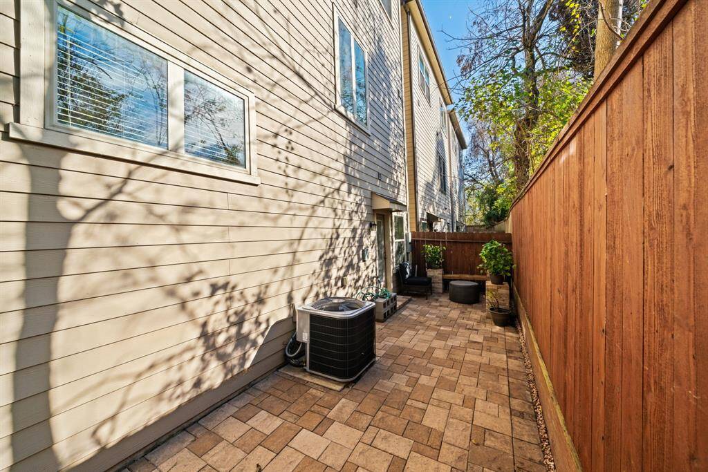 A narrow, private outdoor space with a brick-paved walkway, bordered by a wooden fence. It features an HVAC unit and potted plants, offering a cozy area for relaxation or gardening.