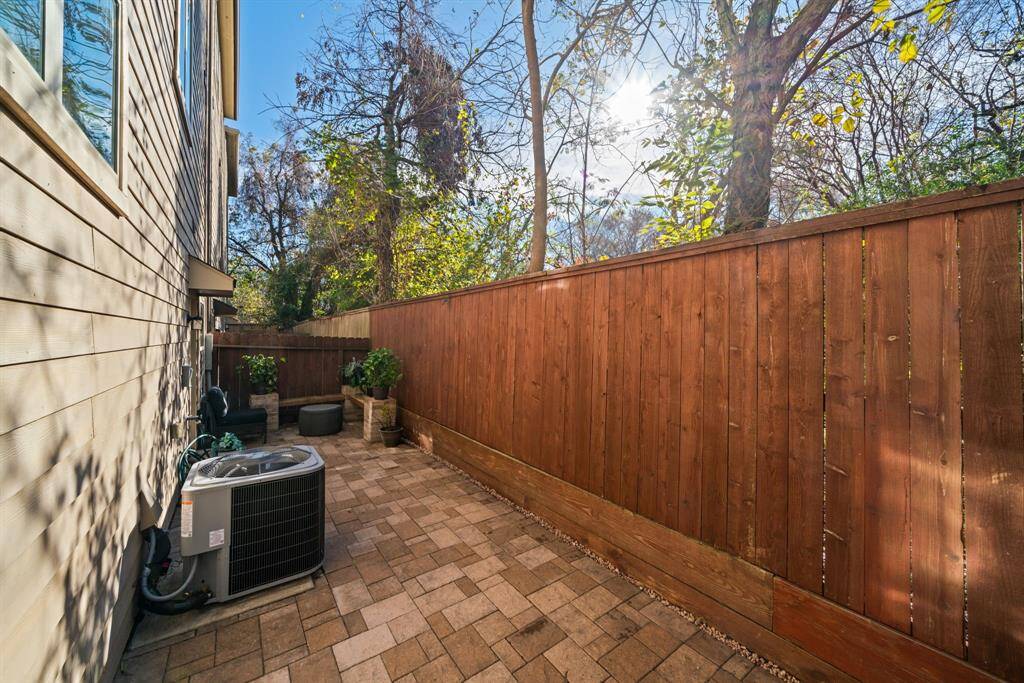 This photo showcases a narrow, paved side yard with a wooden fence and exterior siding. There's an air conditioning unit, a small bench, and some garden hose storage, offering a neat and functional outdoor space.
