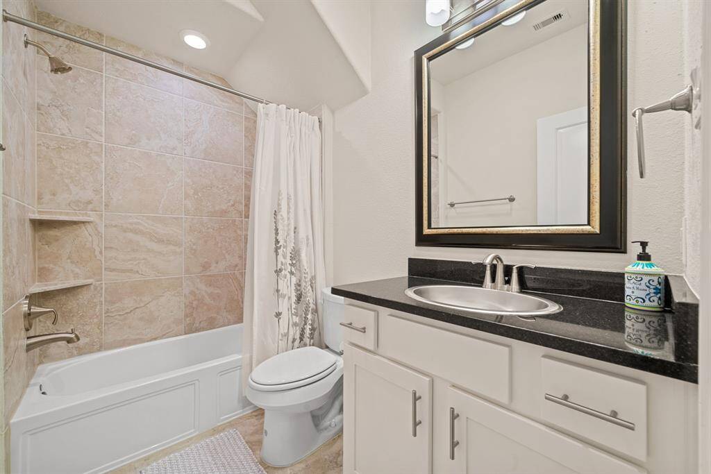 This modern kitchen features a sleek design with white cabinetry, a stylish mosaic backsplash, and stainless steel appliances. A large, black granite island provides ample seating and workspace, accentuated by elegant pendant lighting.