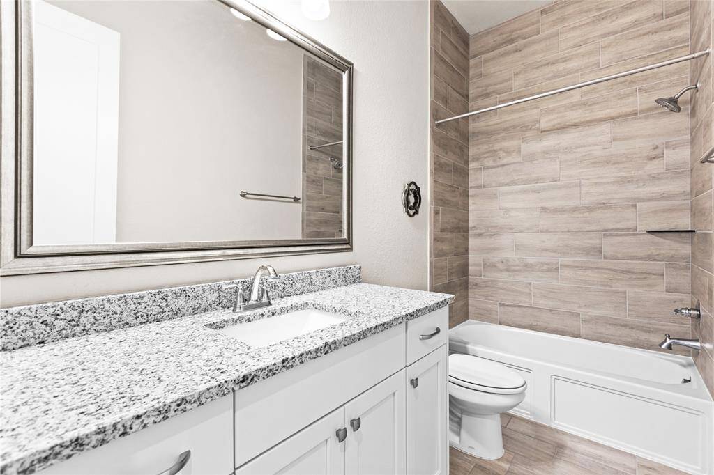 Sleek full bath featuring elegant granite countertops and modern wood-look tile.