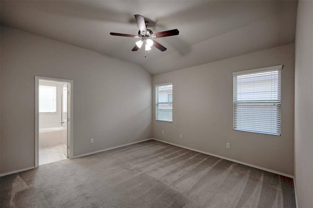 The large primary bedroom is bright with two windows and high ceiling.