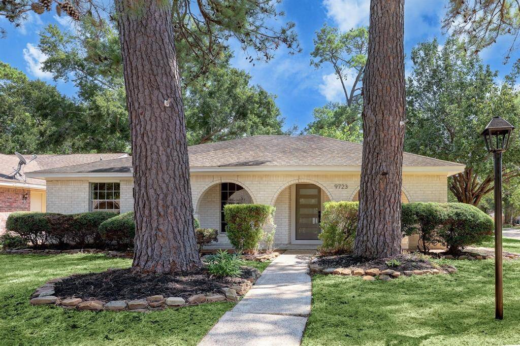 A lasting first impression—this corner-lot home showcases a wide covered front porch framed by graceful brick archways. The expansive front yard is shaded by mature trees.