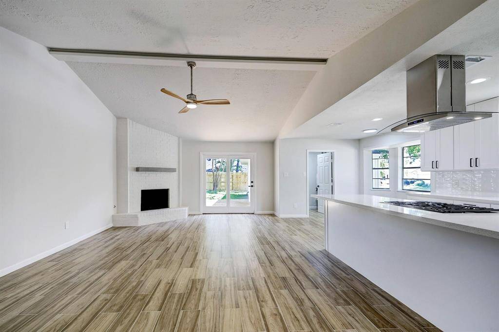 The expansive living room features vaulted ceilings and wood-look flooring. A floor-to-ceiling fireplace with a custom mantle adds warmth and character. The open layout effortlessly connects to the kitchen and breakfast area.