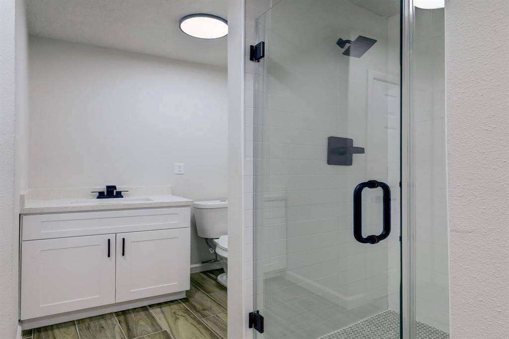Modern and fresh, this full bathroom features a white vanity, a glass-enclosed shower, and black fixtures. Clean tones create a refreshing atmosphere.