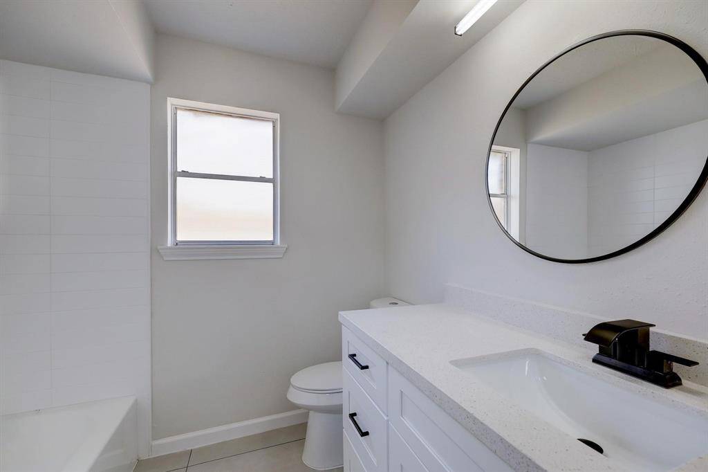 This bathroom includes a stylish vanity with matte black fixtures, a round mirror, and a window that brings in natural brightness—contemporary and functional.