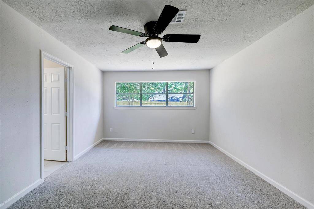 The primary bedroom features a broad window that frames views of the backyard and a modern ceiling fan. The room's proportions offer flexibility for various furniture arrangements.