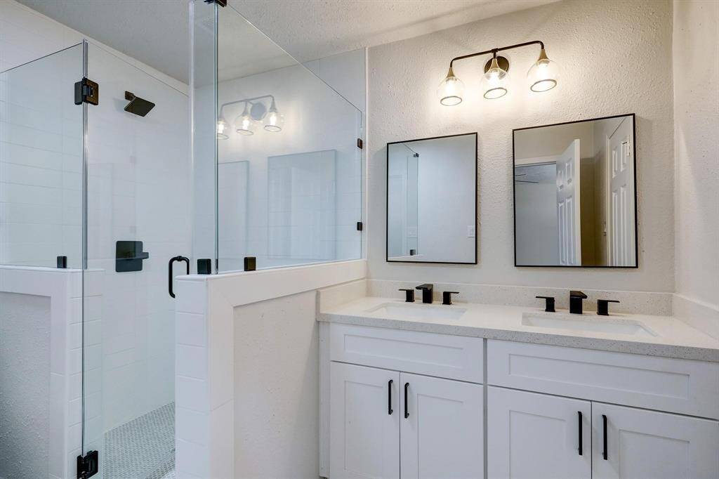 Beautifully updated, the primary bathroom offers dual sinks with black-framed mirrors, coordinating fixtures, and a glass-enclosed shower. A balanced blend of style and functionality.