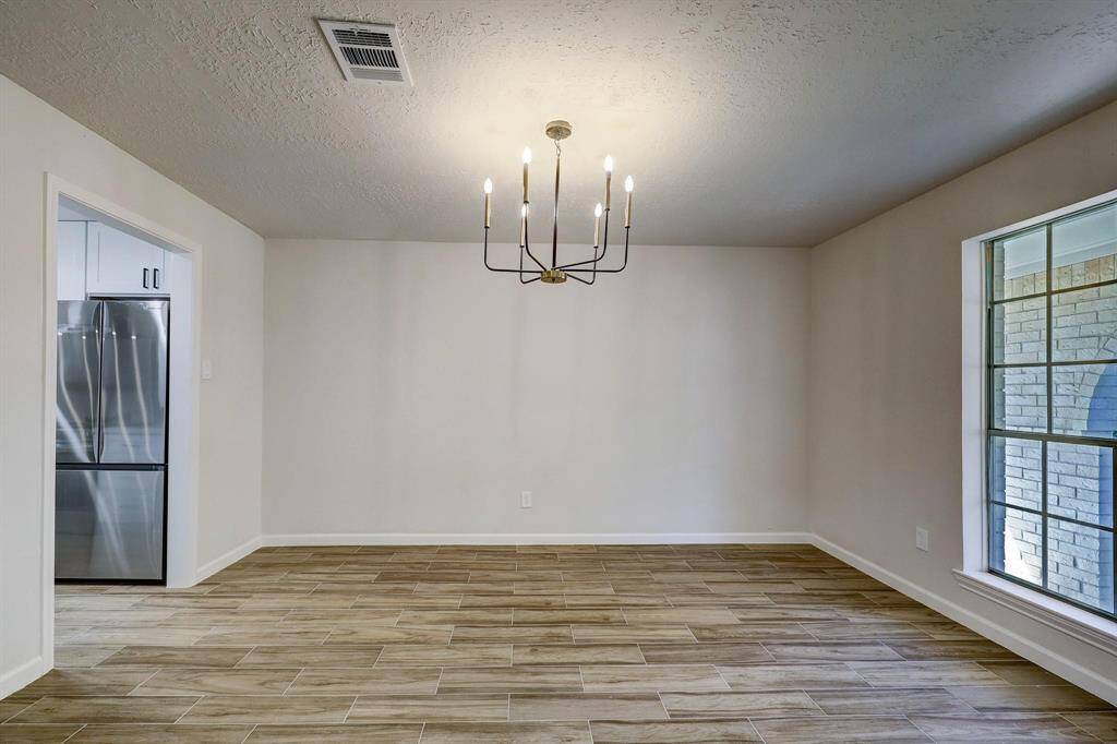 This dining space is brightened by an oversized window and anchored by a contemporary chandelier. The neutral color palette and warm wood-look floors enhance the atmosphere. Direct access to the kitchen makes hosting seamless.