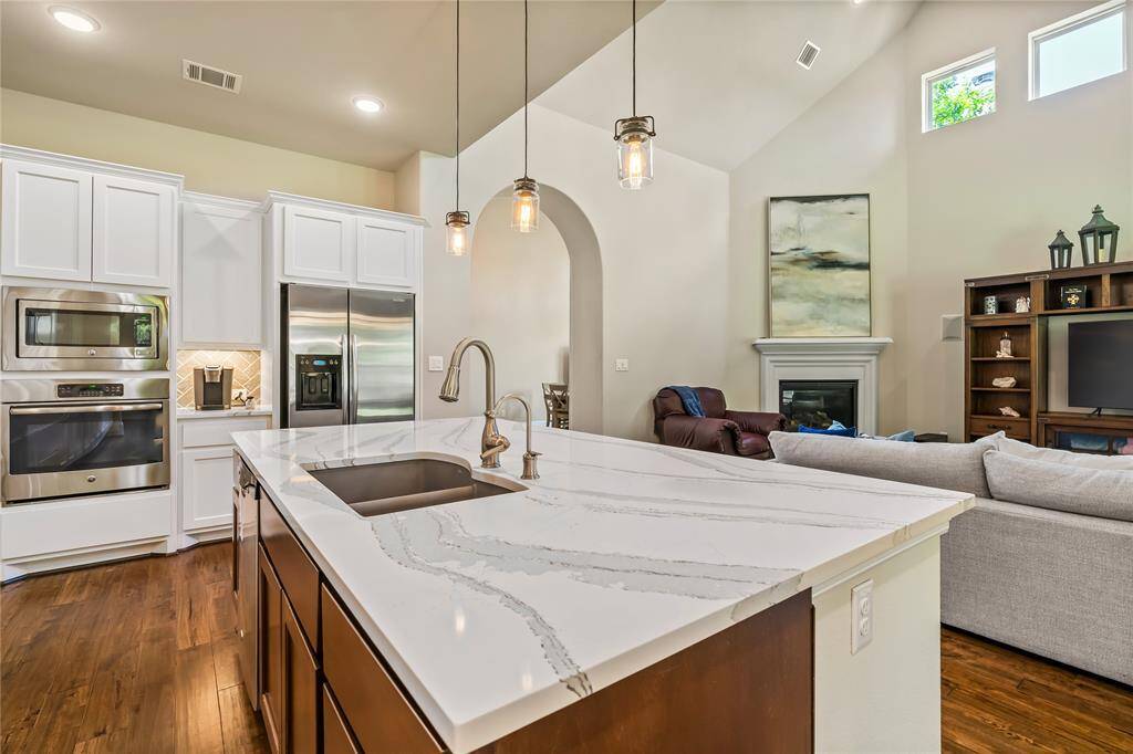 This spacious primary bedroom features hardwood floors, a tray ceiling with a ceiling fan, and large windows offering ample natural light. It includes a comfortable bed, a wall-mounted TV on a vintage desk, and an ensuite bathroom.