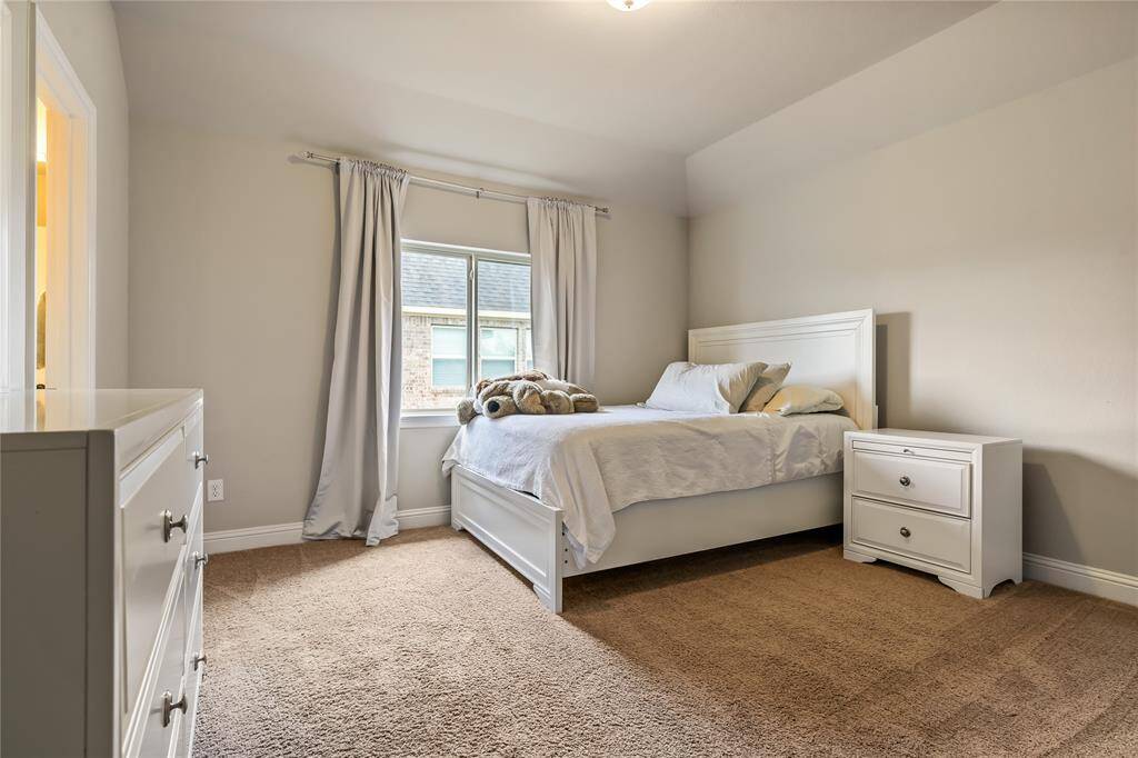 This cozy bedroom features a comfortable bed, a loveseat by a window with plantation shutters, and a TV on an ornate stand. This is an en-suite that would accomadate "PARENTS", nanny, etc.  Private entrance between 3 car and 1 car garages.  A second bed is tucked into a separate nook, adding extra space and privacy. The room is carpeted and tastefully decorated.  And, is ready to add a kitchen.  All material is inside wall (water, electricity and gas).