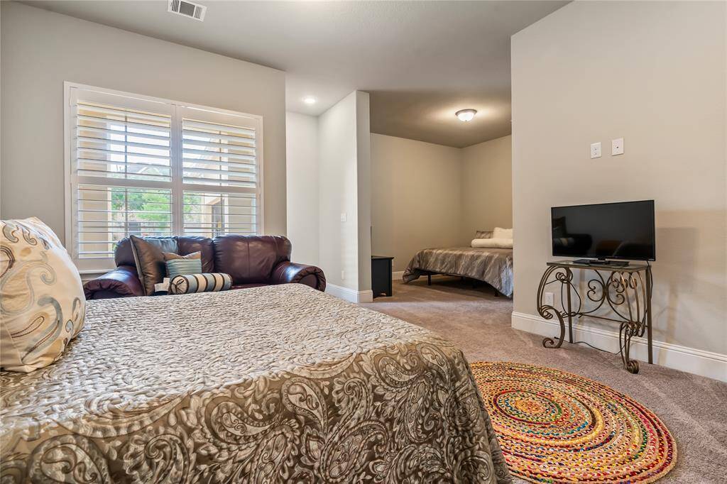 This cozy bedroom features a plush carpet, a comfortable bed with neutral bedding, and a TV on an ornate stand. There's an arched doorway leading to another space, adding a touch of elegance and privacy.  This is an en-suite and would be fantastic living space for "PARENTS", nanny, etc.