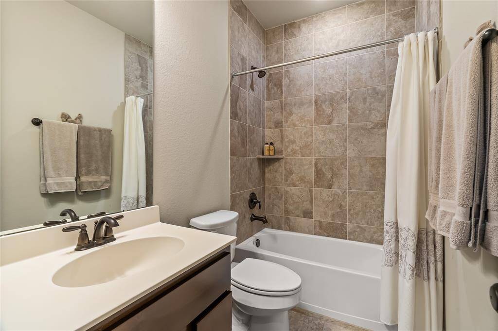 This bathroom features a modern design with a tiled walk-in shower, a sleek glass door, and a vanity with a polished countertop. The neutral tones and bronze fixtures create a warm and inviting atmosphere.
