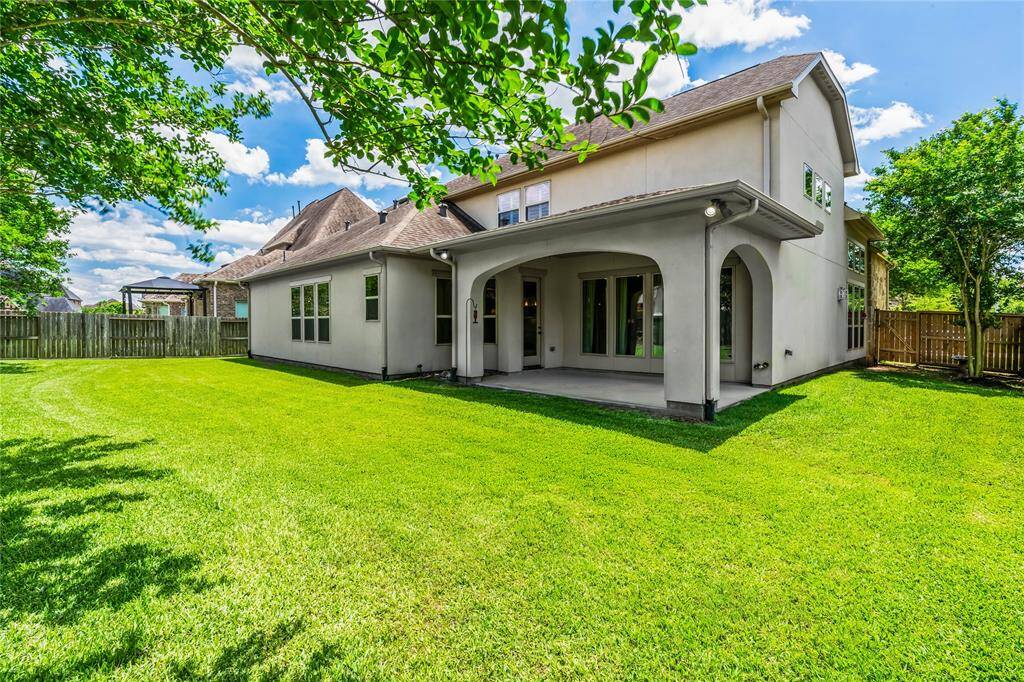 This photo showcases a spacious backyard with a lush green lawn, a covered patio, and a modern two-story house, ideal for outdoor entertaining and relaxation.