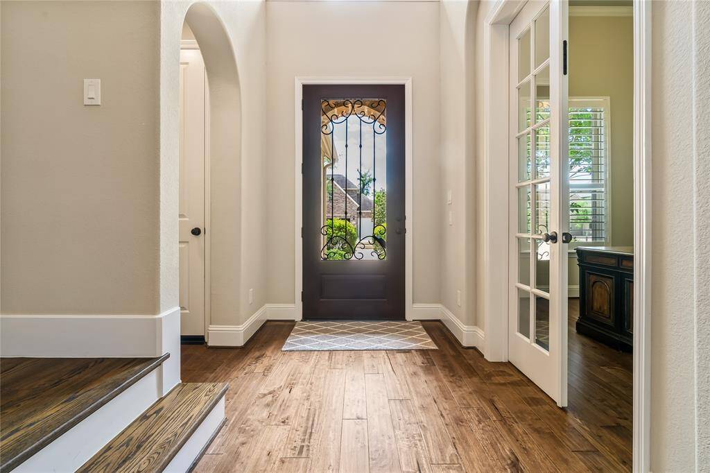This entryway features a stylish wooden door with ornate ironwork, hardwood floors, and natural light streaming through adjacent glass-paneled doors, offering a warm and inviting first impression.