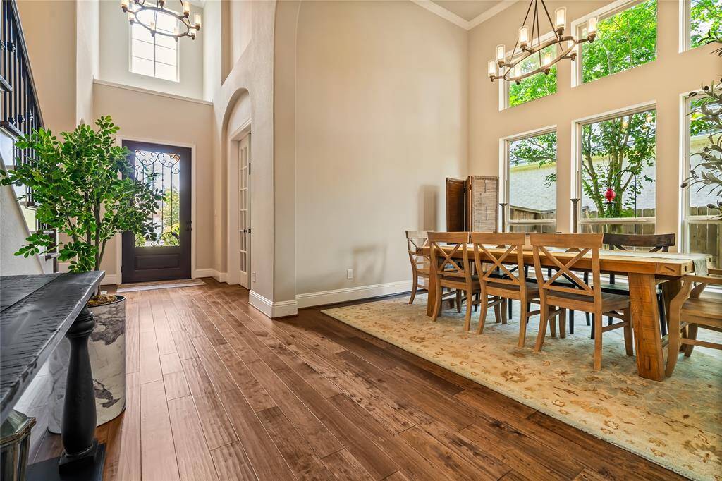 This inviting home features a spacious dining area with high ceilings, large windows providing abundant natural light, and elegant wooden flooring. The entrance showcases a stylish door and decorative lighting, enhancing the home's warm and welcoming atmosphere.