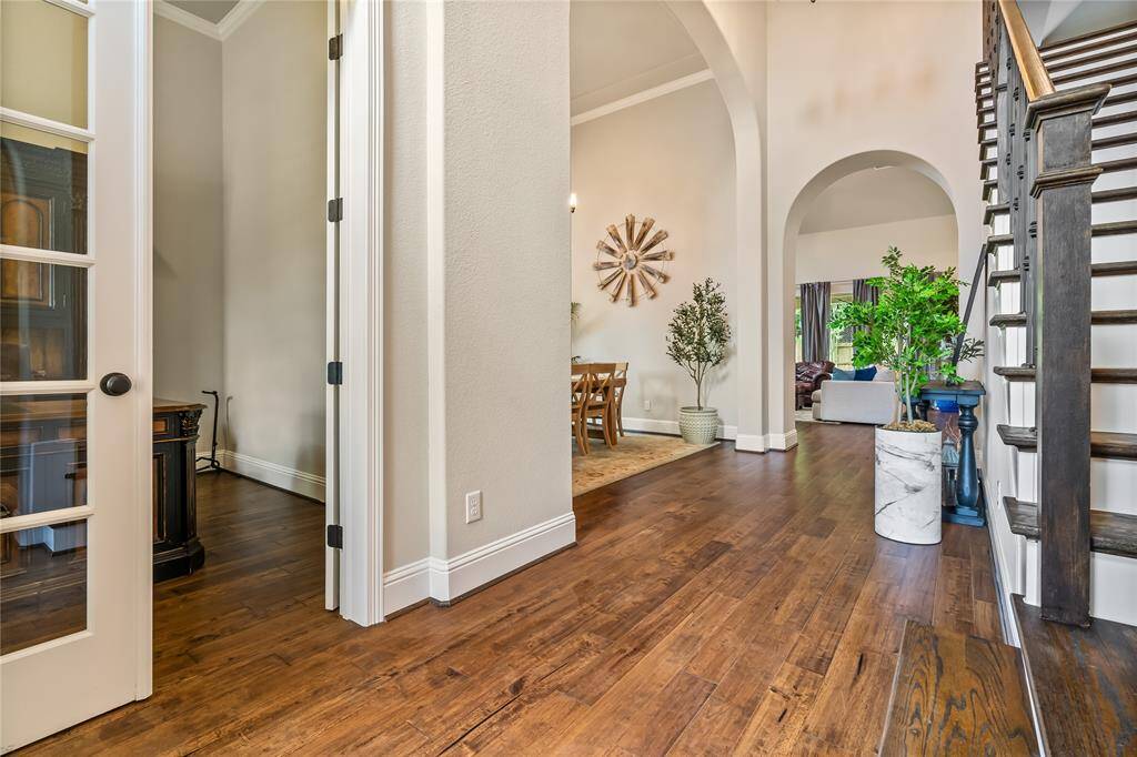This inviting entryway features elegant hardwood floors, high ceilings, and stylish arches leading to a spacious living area. A staircase with dark wood accents complements the bright, airy ambiance.