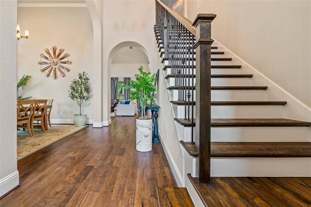 This photo showcases a welcoming entryway with rich hardwood floors and a staircase featuring elegant dark wood and iron railings. The open layout leads to a dining area with stylish decor and a glimpse of a cozy living space, enhanced by an abundance of natural light. Gameroom and secondary bedrooms (with bath rooms) upstairs.