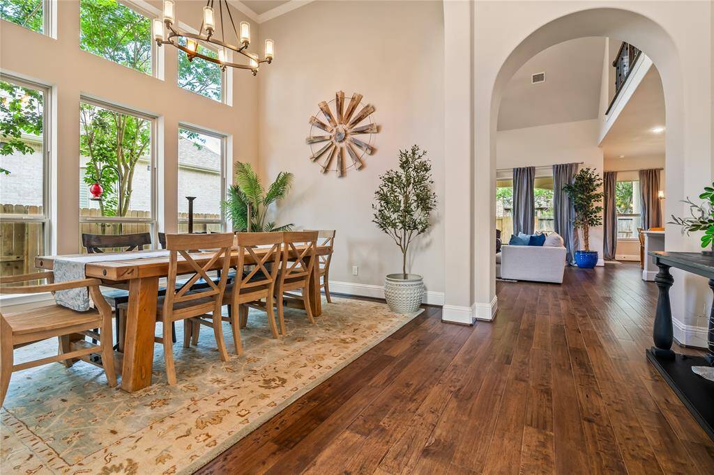 This inviting home features an open dining and living area with high ceilings and large windows, creating a bright and spacious atmosphere. The hardwood floors add warmth, while contemporary decor and greenery offer a stylish touch. Perfect for entertaining and family gatherings.