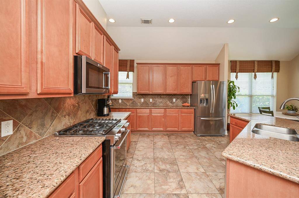 This is a cook's dream kitchen, with honey colored cabinetry everywhere, up and down; plentiful and useful! Anywhere you land in tasking, there's a convenient feature to help and comfort you. Creamy earth toned granite counter tops are complemented by the mottled tile backsplash, with shining appliances adding to the glow of this space.
