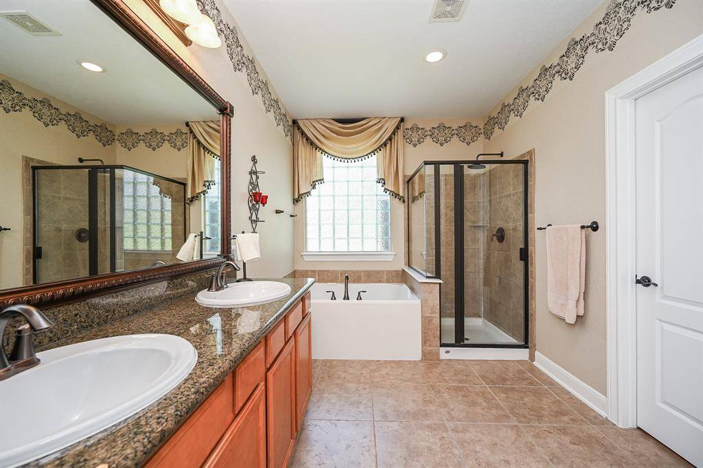 This gorgeous ensuite bath will relax you, just by walking in! Deep granite counters host warm cabinetry below dual sinks, sophisticated framed wall mirror, and walk-in shower and garden tub, side-by-side, under a big window, adorned with art-deco like glass.