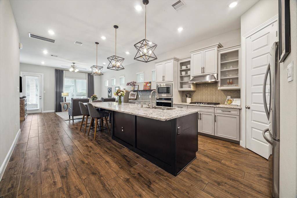 This stunning, light-filled kitchen boasts warm tones, exquisite tile, and sleek granite countertops, creating an ideal space for all your culinary creations. Admire the beautiful cabinetry and rich hardwood tile flooring, carefully selected for both style and function. The sellers worked directly with the builder to choose premium upgrades, including the elegant tile backsplash, deluxe cabinetry, and glass-fronted cabinets, adding an extra touch of sophistication and charm.
