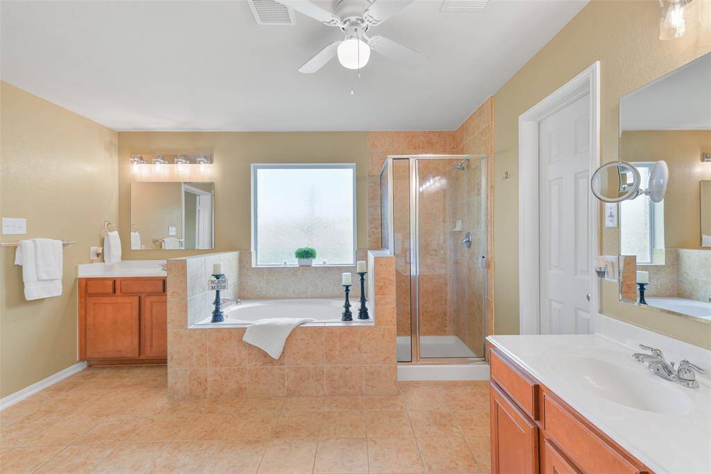 Relaxation awaits in the master bathroom, showcasing separate his & hers vanities with cultured marble countertops, basin sinks, handsome wood cabinetry, new beveled edge mirrors, stylish lighting, a garden tub, and a separate glass-enclosed shower.