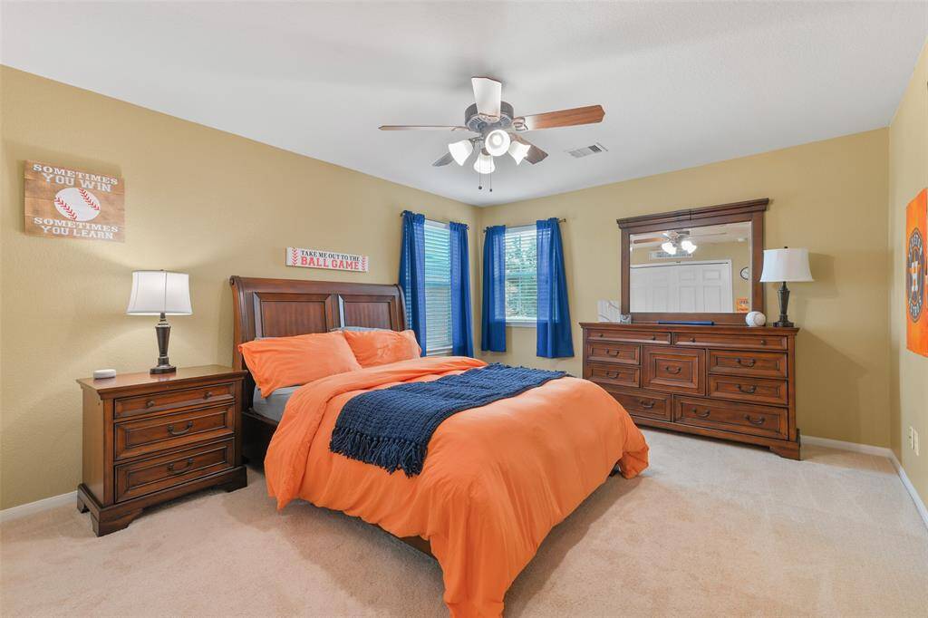 In another generously proportioned secondary bedroom, note the lighted ceiling fan, bright corner windows with front yard views, a lighted ceiling fan, plush carpet, and alighted ceiling fan.
