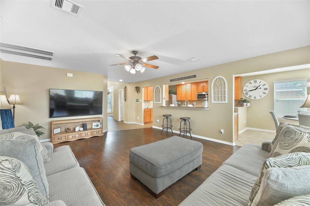 If you continue straight ahead from the entrance, the foyer spills into this comfortable family room that boasts a lighted ceiling fan, neutral paint, luxury laminate plank floors, and a raised bar for extra seating or serving space.