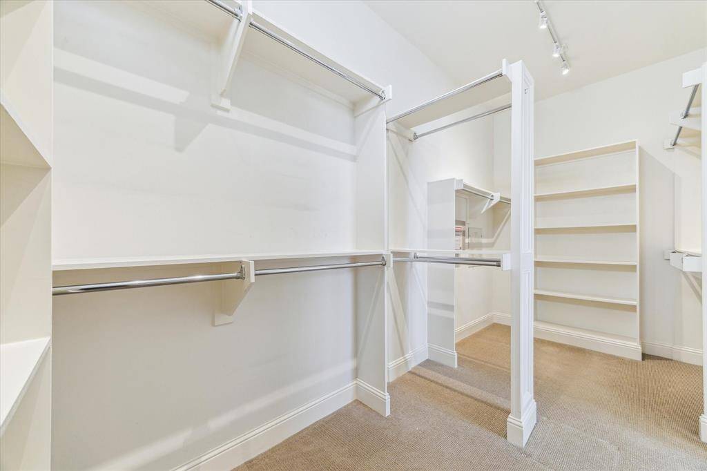 This photo shows a spacious walk-in closet with ample hanging space, built-in shelves, and neutral carpeting, perfect for organized storage.
