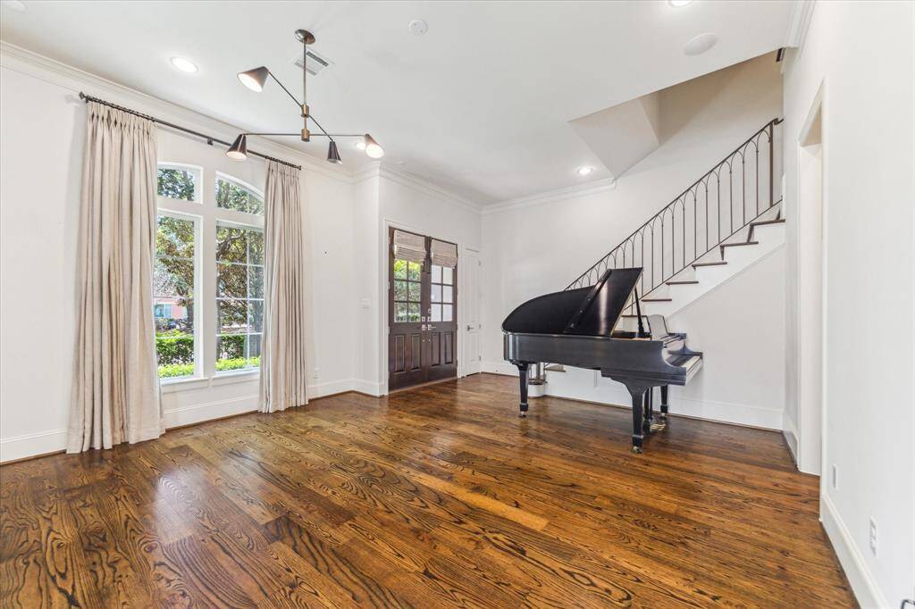 This spacious entryway features elegant hardwood floors, a grand staircase with a sleek railing, and large windows that let in plenty of natural light.