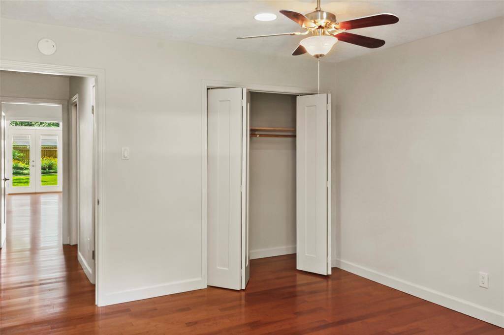 Bright bedroom with hardwood floors, a ceiling fan, and a closet. It opens to a hallway leading to a room with glass doors and a view of a lush garden.