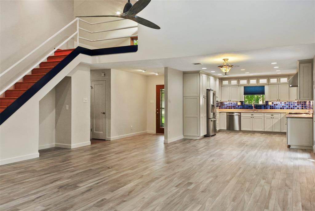 This open-concept home features a modern kitchen with stainless steel appliances and vibrant blue tile backsplash, adjacent to a spacious living area with light porcelain tile wood look flooring. A stylish staircase with a bold accent leads to the upper level, enhancing the contemporary feel.