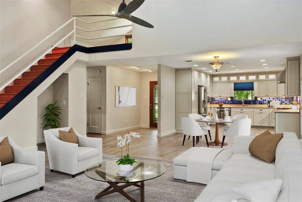This inviting open-concept living space features a modern kitchen with stainless steel appliances and a cozy dining area.  A staircase leads to the upper level, and large windows provide ample natural light. Perfect for entertaining and family living.