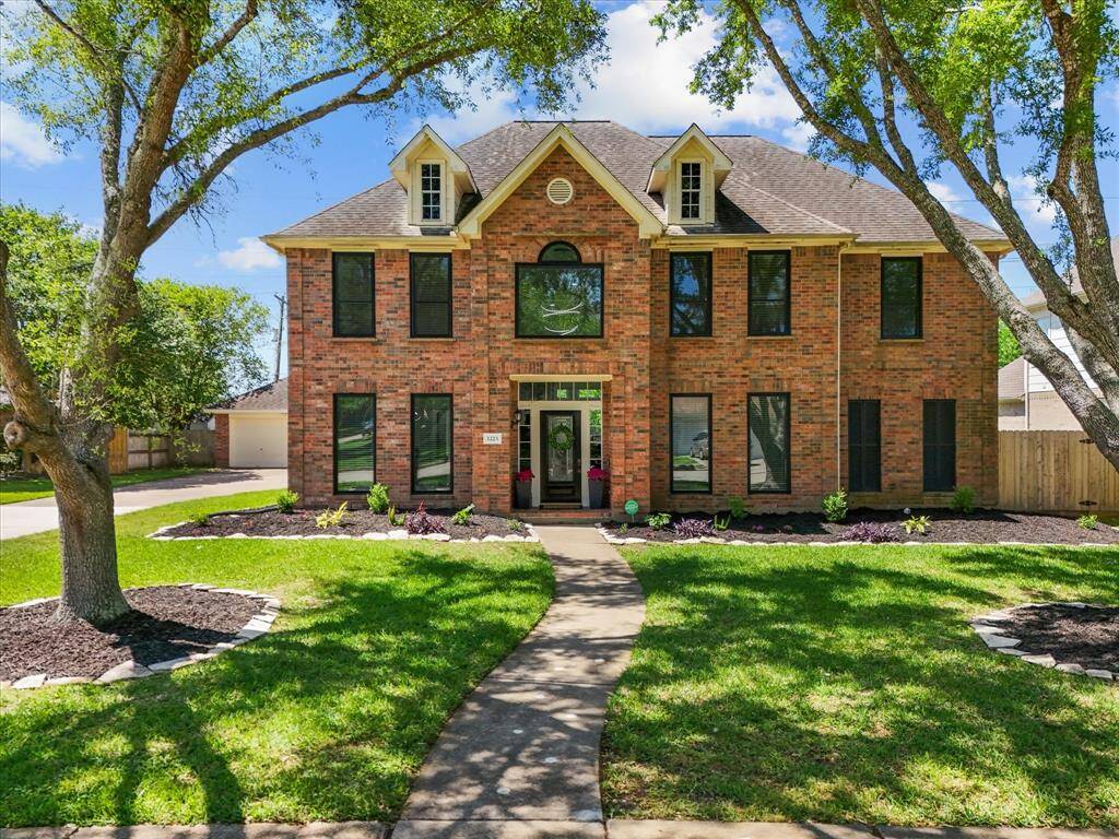 This beautiful two-story brick home features a symmetrical facade with large windows and dormers, framed by mature trees. The well-maintained front yard and curved walkway lead to a welcoming entrance, offering great curb appeal in a peaceful neighborhood setting.