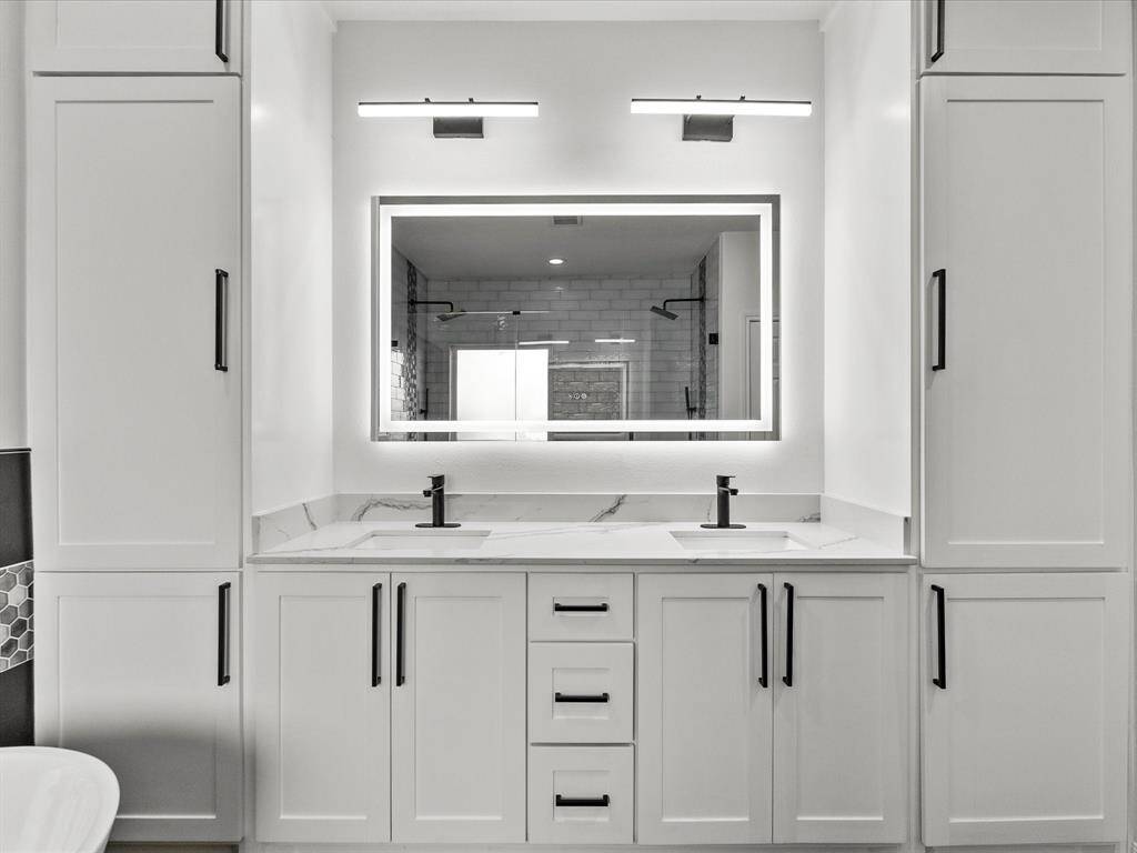 Elegant bathroom vanity with sleek white cabinetry, dual sinks, and a large illuminated mirror.
