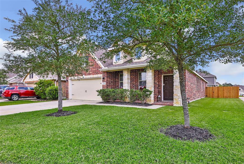 Charming brick home sits on a corner lot with a well-maintained front yard, mature trees, and a two-car garage. Features include a welcoming porch and a spacious driveway.