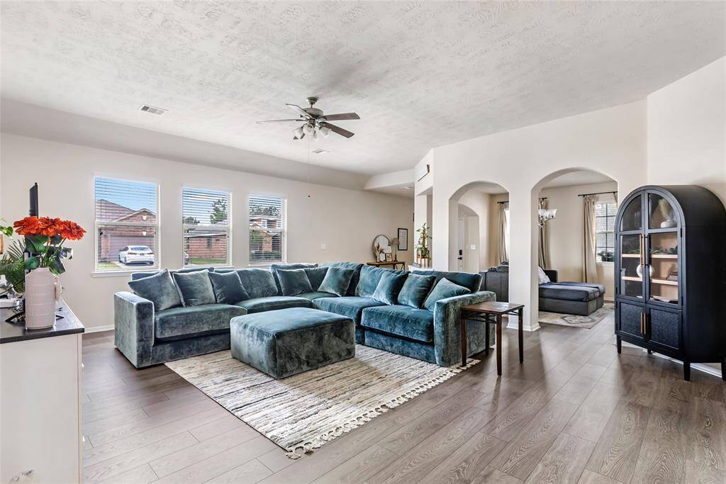 This spacious living room has abundant natural light from multiple windows, and stylish arched doorways. It boasts hardwood floors, modern decor, and a ceiling fan, creating a welcoming and comfortable environment.
