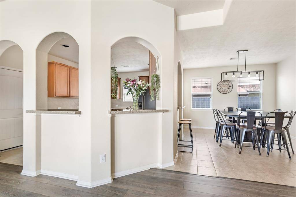 Open-concept dining area with arched openings, offering a view into the kitchen. The space features wood and tile flooring, modern lighting, and a dining table with ample seating, creating an inviting atmosphere.