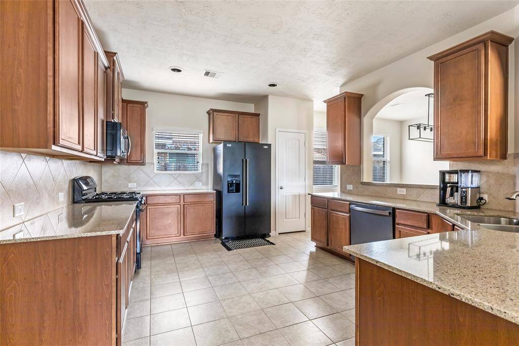 Spacious kitchen featuring light brown cabinets, granite countertops, and stainless steel appliances. The room is well-lit with natural light from multiple windows, and includes a convenient open archway to the dining area.
