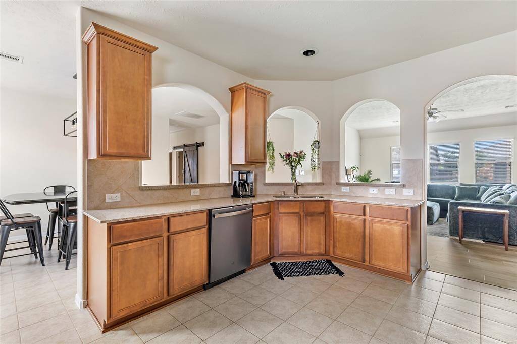 Spacious kitchen with warm wood cabinets and tile flooring, featuring a modern appliance and a cozy breakfast bar. Arched openings connect to a bright living area, enhancing the open layout.