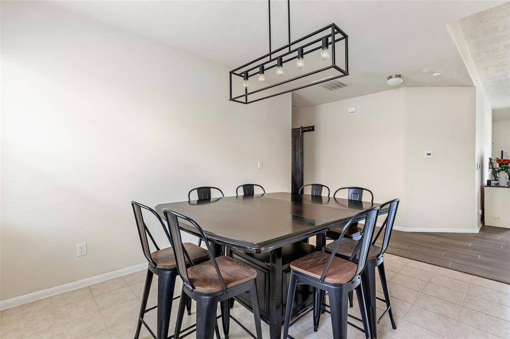 This dining area features a contemporary light fixture above, neutral tile flooring, and opens into a hallway with hardwood floors, creating a seamless flow into the home.