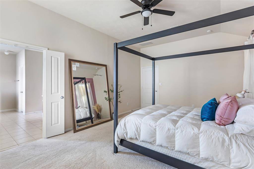 Spacious bedroom with neutral tones features a ceiling fan, and ample natural light. Doorway leading to tiled area enhances the open feel.