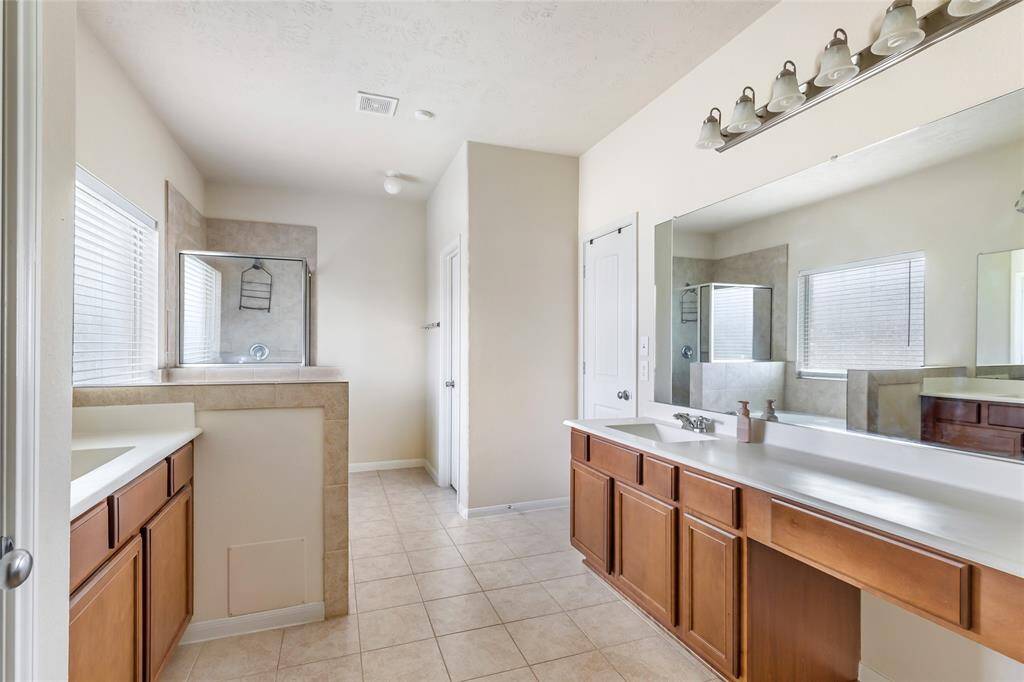 This bathroom features a spacious layout with a large vanity and ample cabinet space. It has a walk-in shower with tile surround, two windows for natural light, and neutral tile flooring.