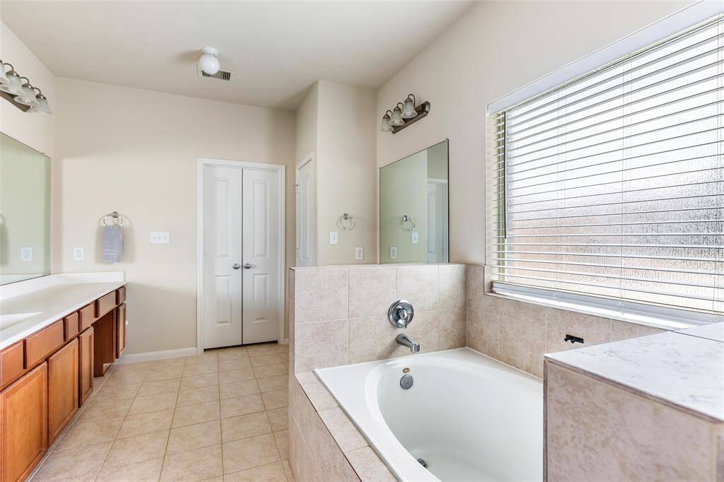 This bathroom features a spacious layout with a large bathtub, double vanity with ample counter space, and a window offering natural light. The neutral tile flooring and soft wall colors create a relaxing atmosphere.