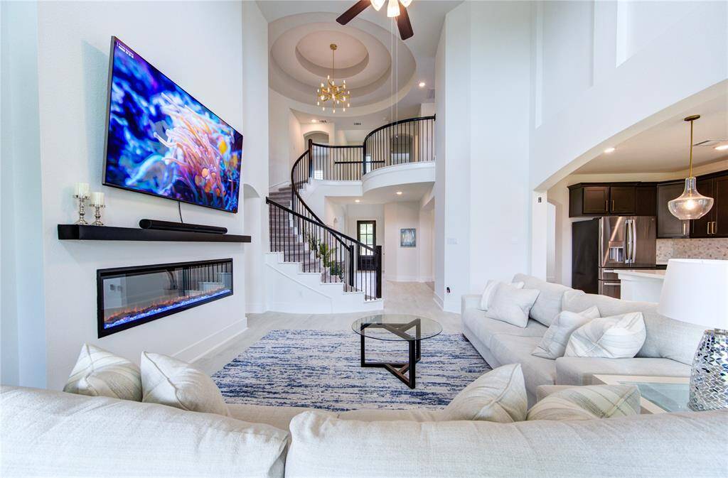 Luxurious den featuring soaring ceilings, a modern fireplace, and a sleek staircase, perfect for relaxation and entertainment.